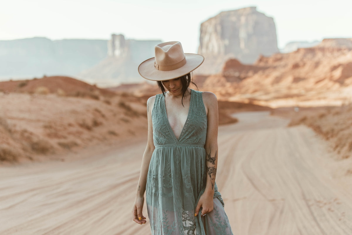 woman in blue sleeveless dress wearing white cowboy hat walking on brown sand during daytime