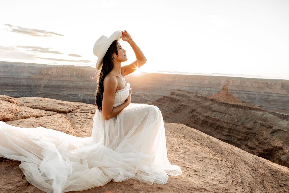 A woman in a white dress and hat sitting on a rock