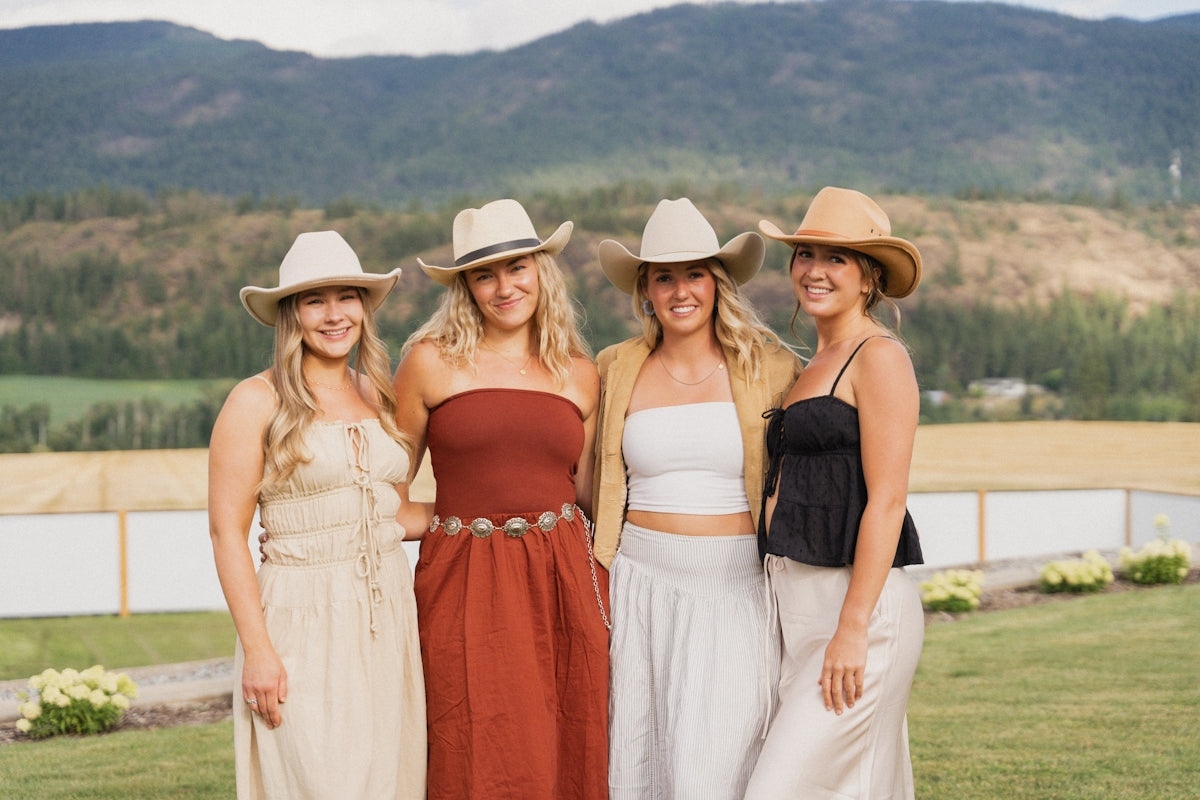 Four women pose in cowboy hats outdoors.